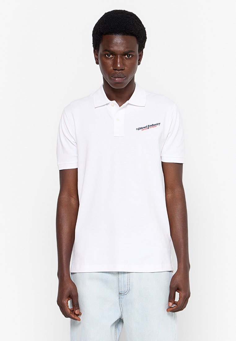 Weißes Poloshirt aus Baumwolle mit Kragen und kurzen Ärmeln. Mit einem roten und schwarzen Logo auf der linken Brustseite.