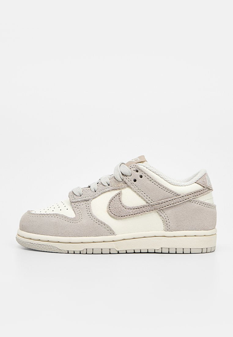 Niedriger Sneaker mit beigen Wildleder- und weißen Lederpaneelen, grauen Schnürsenkeln und beigem Nike-Swoosh-Logo auf weißem Hintergrund.