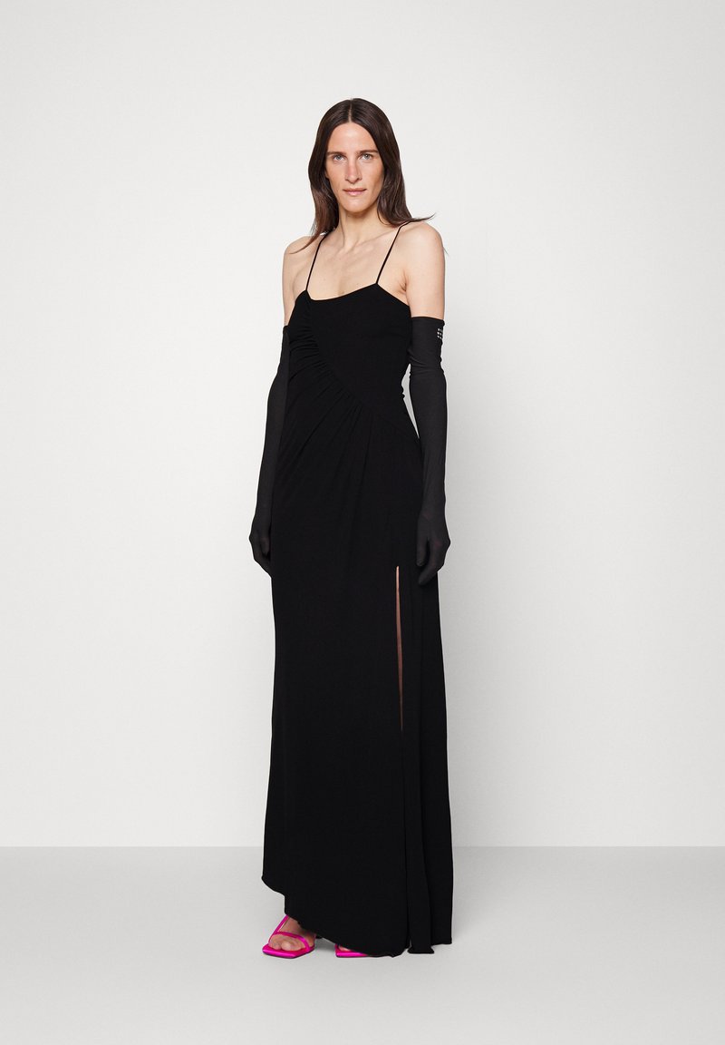 Schwarzes Maxikleid mit Raffung an der Brust, dünnen Trägern und einem seitlichen Schlitz, kombiniert mit langen schwarzen Handschuhen und rosa Riemchensandalen.