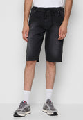 Mann in schwarzen knielangen Shorts, weißen Socken, grauen Sneakern und einem weißen Shirt vor einem schlichten Hintergrund.
