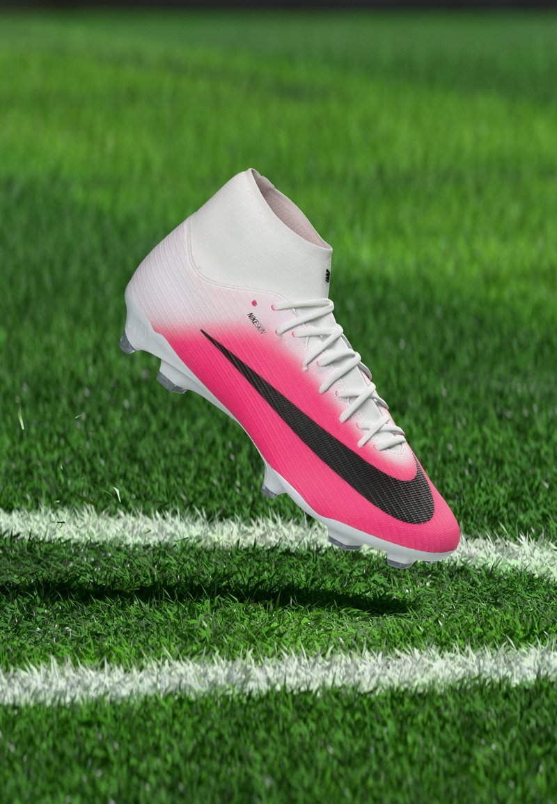 Weißer und pinker Fußballschuh mit schwarzem Swoosh, der über einem grünen Spielfeld nahe einer weißen Begrenzungslinie schwebt.