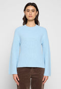 Helles blaues gestricktes Sweatshirt mit langen Ärmeln, geripptem Muster, rundem Ausschnitt und legerem Schnitt. Getragen über braunen Cord-Hosen.