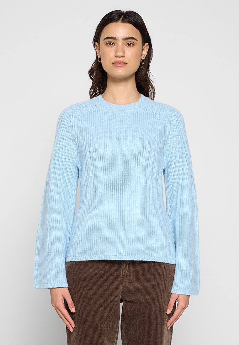 Helles blaues gestricktes Sweatshirt mit langen Ärmeln, geripptem Muster, rundem Ausschnitt und legerem Schnitt. Getragen über braunen Cord-Hosen.
