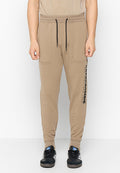 Beige Jogginghosen aus weichem Material, mit einem elastischen Bund und Kordelzug, seitlichen Taschen und einem schwarzen Logo entlang des linken Beins.