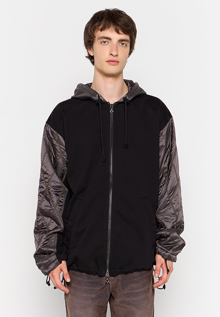 Schwarzer Hoodie mit grauen gesteppte Ärmeln, Reißverschluss, verstellbare Kapuze mit Kordelzug und Fronttaschen. Weicher Stoff mit sportlichem Design.