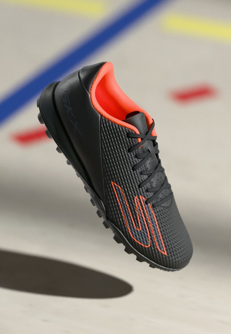 Schwarze Fußballschuhe aus strukturiertem Synthetikmaterial, mit orangefarbenen Akzenten, Schnürdesign und einer genoppten Gummi-Außensohle.