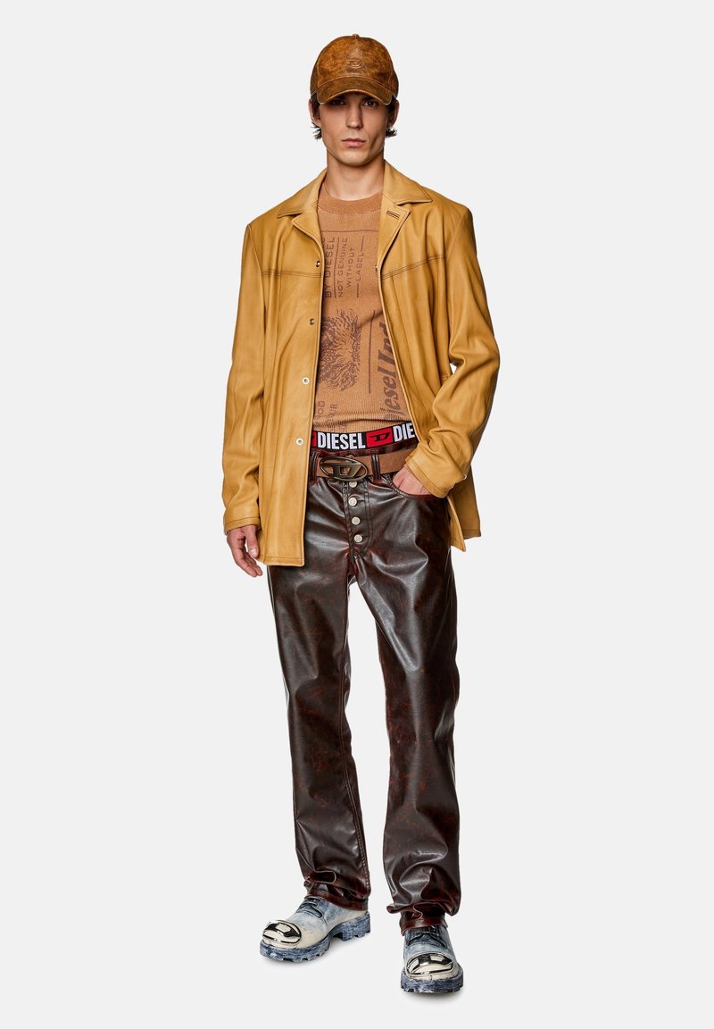 Hellbraune Lederhemdjacke, braunes gemustertes Tanktop, glänzende braune Hose, schwarzer Gürtel mit silberner Hardware, blaue und graue klobige Schuhe.