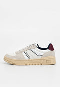 Herrensneaker mit weißem Lederobermaterial, beigen Wildlederakzenten, schwarzen und roten Details, strukturierter Sohle und Logo an der Seite.