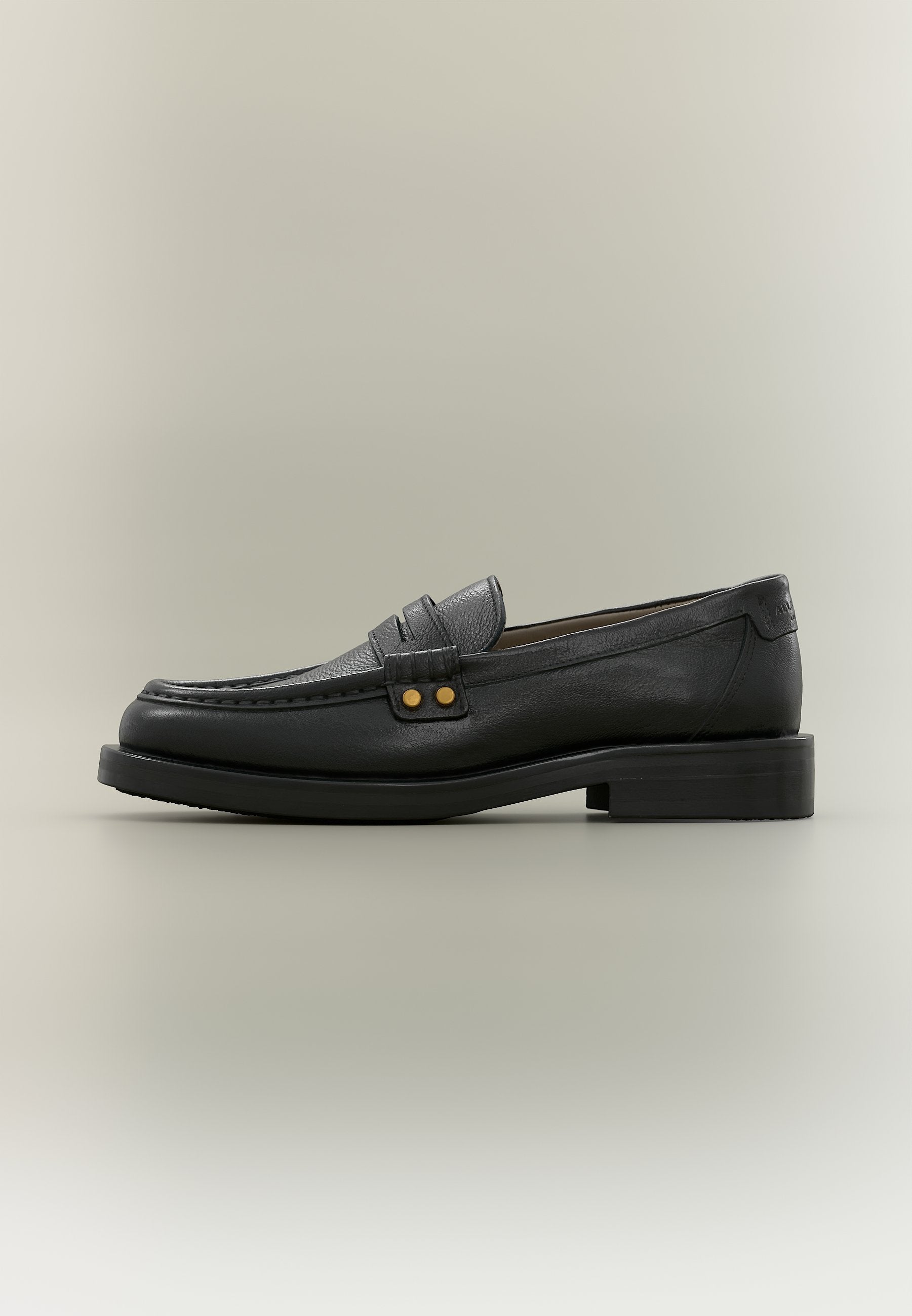 Schwarzer Herrenschuh aus Leder mit Mokassinnaht, dekorativem Riemen mit zwei goldenen Nieten und niedrigem, geschichtetem Absatz auf neutralem Hintergrund.