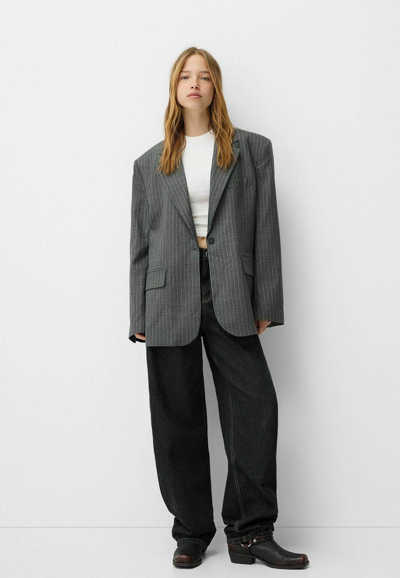 Grauer Nadelstreifen Oversized-Blazer mit zwei Fronttaschen, kombiniert mit lockeren, dunklen Jeans und klobigen schwarzen Ankle Boots. Darunter ein einfaches, weißes Cropped-Top.