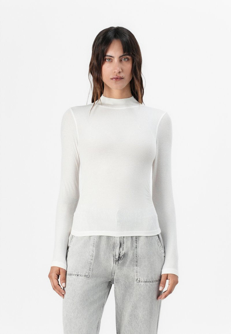 Weißes Langarm-T-Shirt aus geripptem Material mit hohem Ausschnitt und schmaler Passform, kombiniert mit hellgrauen, weiten Jeans.
