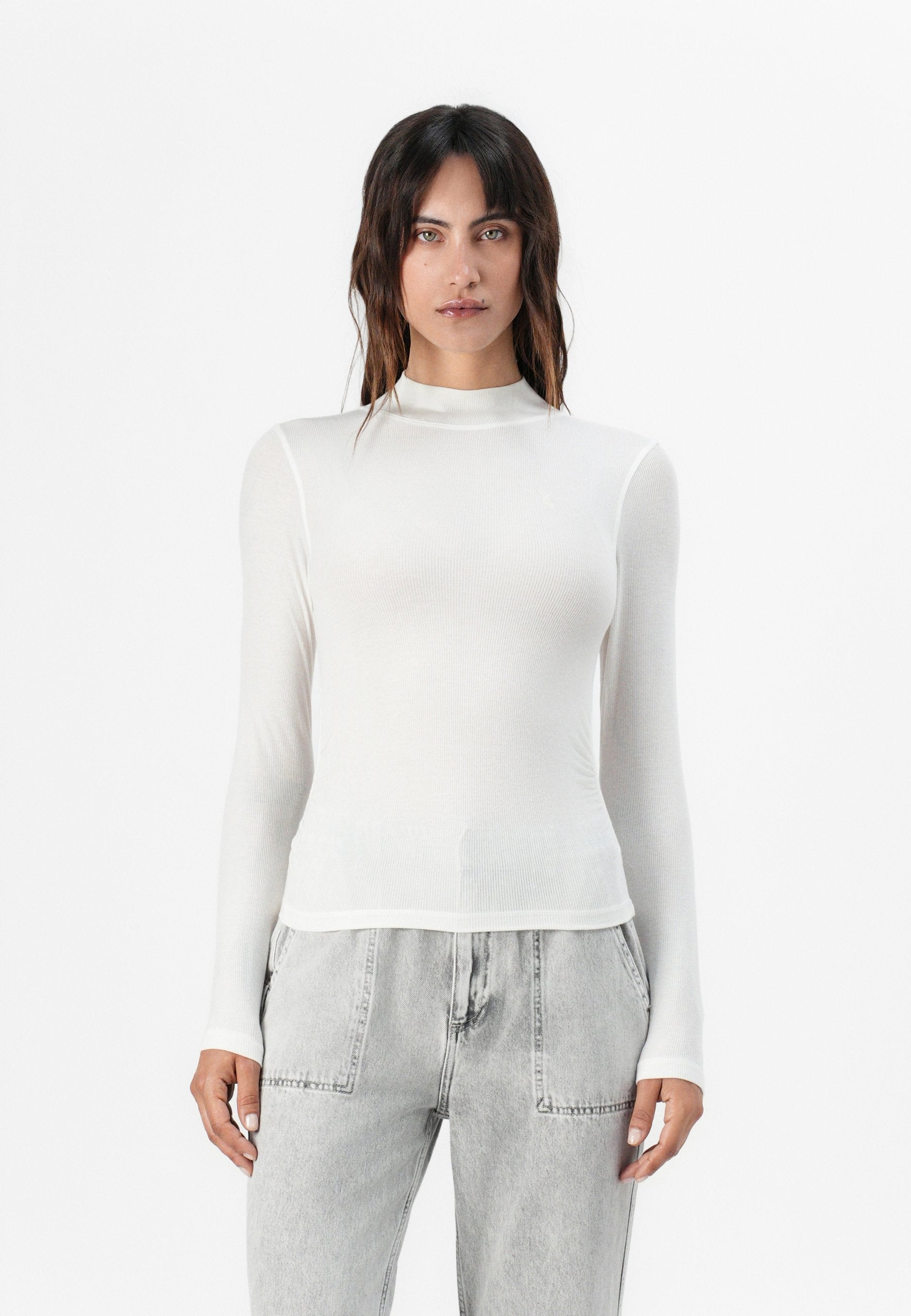 Weißes Langarm-T-Shirt aus geripptem Material mit hohem Ausschnitt und schmaler Passform, kombiniert mit hellgrauen, weiten Jeans.