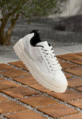 Weiße Leder-Sneaker mit schwarzem Innenleben, dicker geriffelter Sohle und auffälligem Schnürdesign. Verfügt über ein minimales Logo an der Seite.