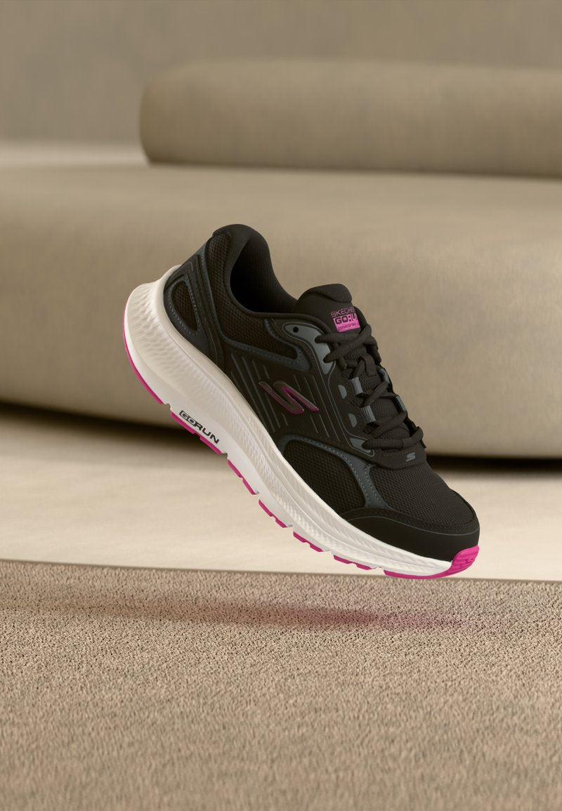 Schwarzer Sportschuh mit einem Obermaterial aus Mesh, weißer und pinker Sohle sowie strukturierten Akzenten. Verfügt über Schnürsenkel und ein Logo an der Seite.
