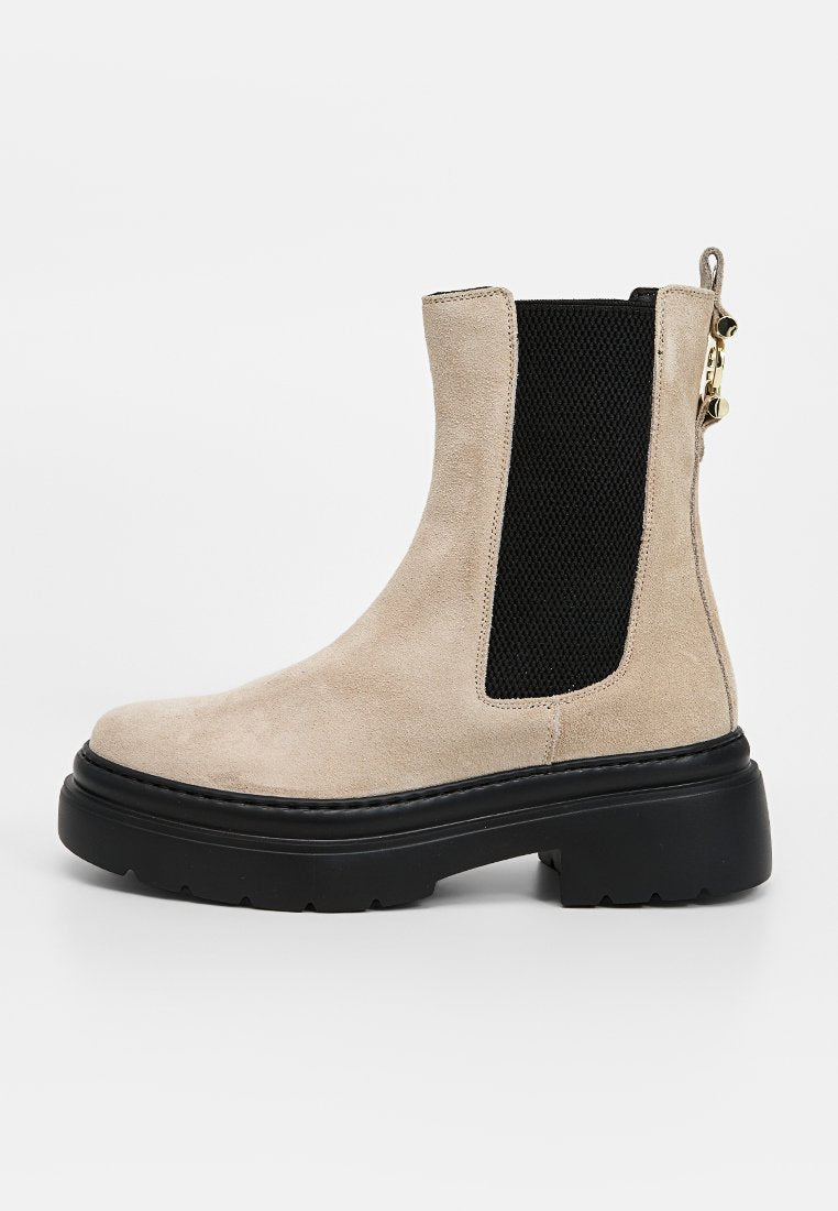 Beiger Wildleder-Stiefelette mit schwarzem elastischem Seiteneinsatz, klobiger schwarzer Sohle und Reißverschluss. Glatte Textur und schlankes Design.