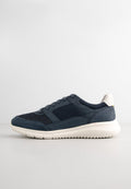 Marineblaue Sneakers aus einer Mischung von Mesh- und Wildledermaterialien, mit einer weißen Laufsohle und einem kleinen gelben Akzent nahe der Ferse. Strukturiertes Design.