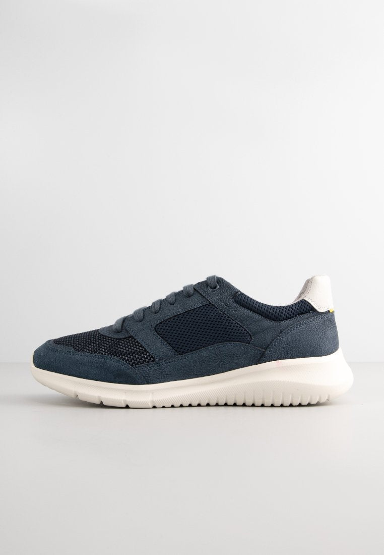 Marineblaue Sneakers aus einer Mischung von Mesh- und Wildledermaterialien, mit einer weißen Laufsohle und einem kleinen gelben Akzent nahe der Ferse. Strukturiertes Design.