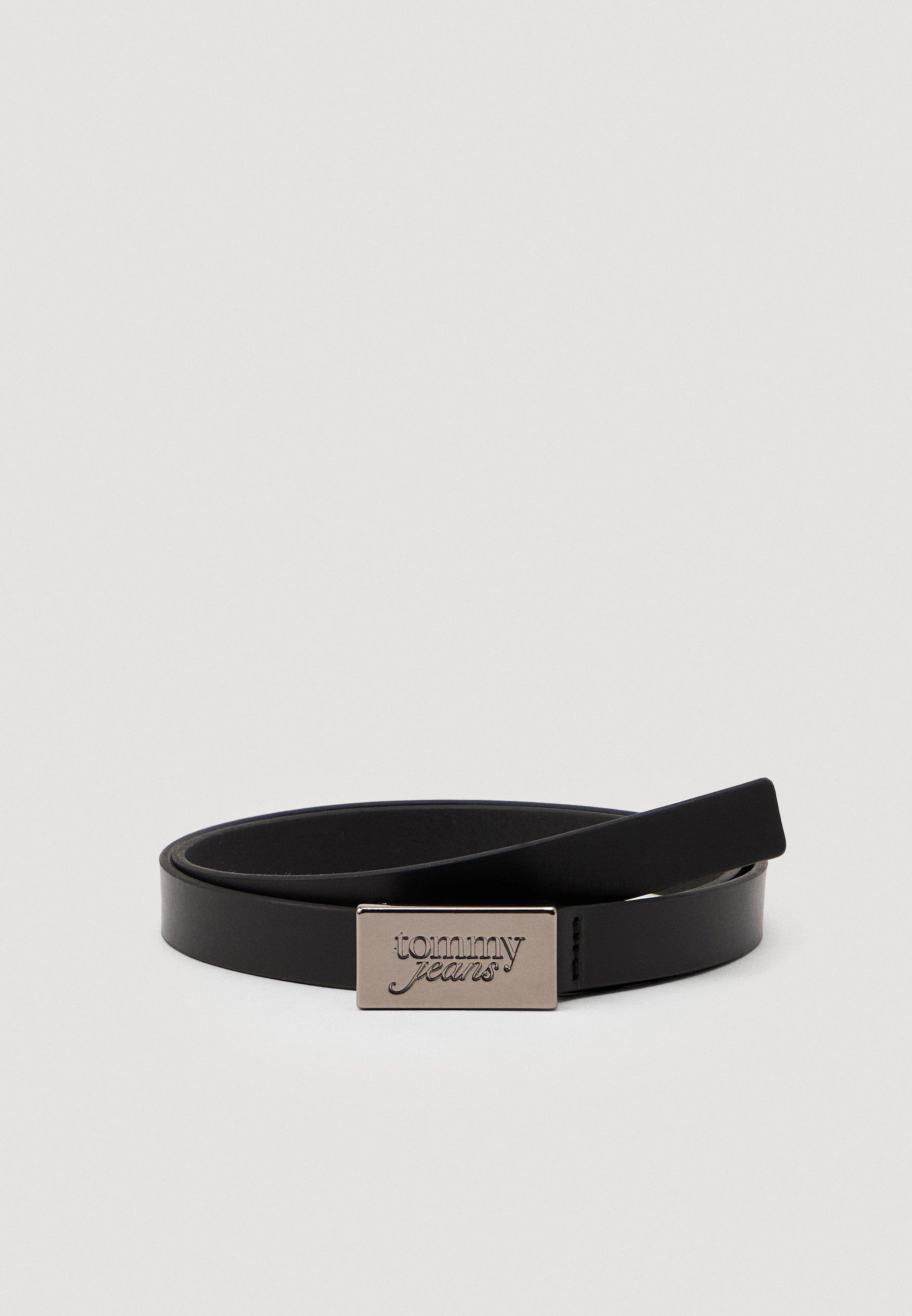Schwarzer Lederhut mit einem eleganten Design, ausgestattet mit einer rechteckigen silbernen Schnalle, die mit "tommy jeans" geprägt ist. Glatte Textur, minimalistischer Stil.