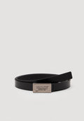 Schwarzer Lederhut mit einem eleganten Design, ausgestattet mit einer rechteckigen silbernen Schnalle, die mit "tommy jeans" geprägt ist. Glatte Textur, minimalistischer Stil.