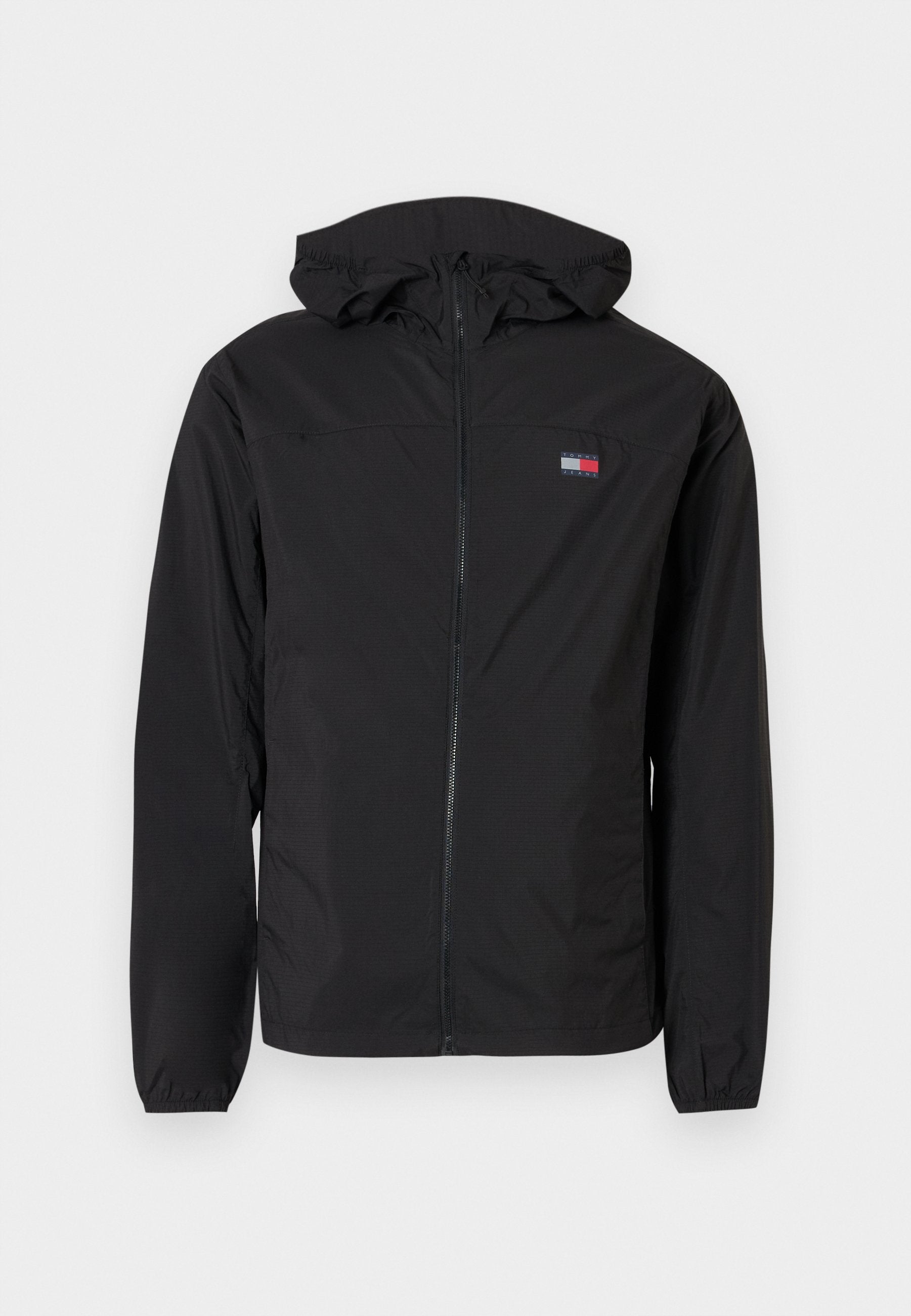 Schwarze, leichte Jacke mit durchgehendem Reißverschluss, Kapuze und elastischen Bündchen. Mit einem Logo-Patch auf der linken Brust. Glatte Textur.