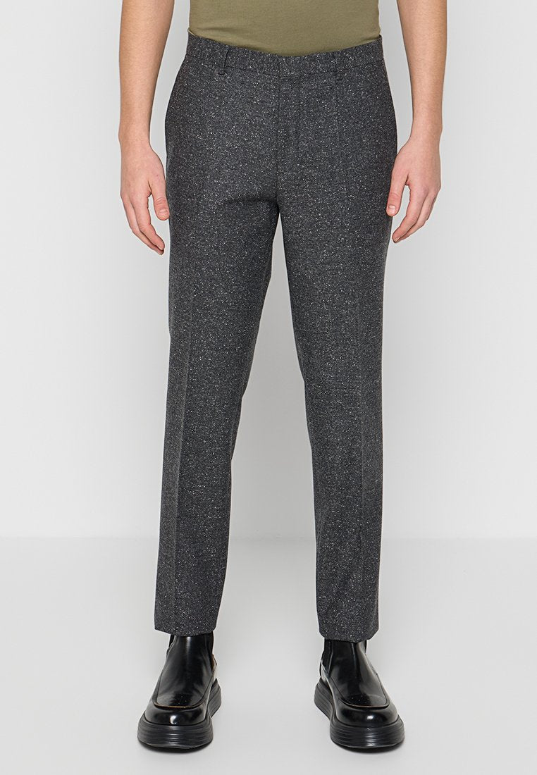 Graue, strukturierte Hose mit einem dezenten gesprenkelten Muster, tailliertem Schnitt und normalem Bund. Kombiniert mit glänzend schwarzem Schuhwerk.