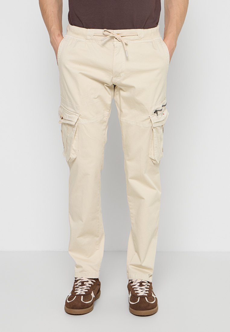 Beige Cargohosen mit Kordelzug in der Taille und mehreren Taschen, getragen mit braunen Sneakers und einem dunkelbraunen Hemd.