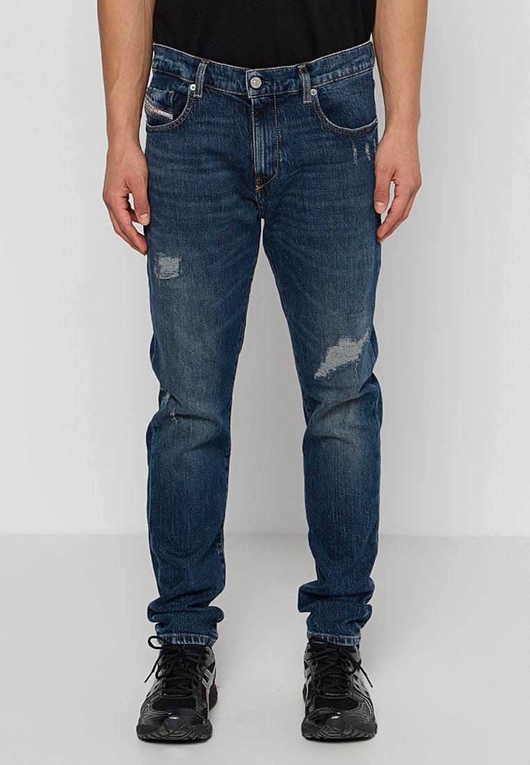 Blaue Jeans aus Denim im Slim-Fit-Schnitt, mit zerstörten Patches und leichter Ausbleichung. Abgeschlossen mit einem klassischen Fünf-Taschen-Design und Knopfverschluss.