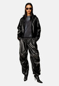Schwarze Lederkapuzenjacke und weite Hosen, kombiniert mit einem enganliegenden schwarzen Oberteil. Accessoires sind dunkle Sonnenbrillen und spitze schwarze Absätze.