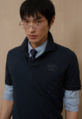 Marineblaues Poloshirt mit gesticktem "DIESEL ONLY THE BRAVE" Logo. Übereinander getragen über einem hellblauen Hemd mit klassischem Kragen und kurzen Ärmeln.