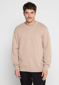 Beige Strickpullover mit strukturiertem Rippdesign, Rundhalsausschnitt, langen Ärmeln und einem kleinen Logo auf der Brust, kombiniert mit dunklen Hosen.