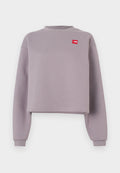 Lila kurz geschnittenes Sweatshirt mit langen Ärmeln, geripptem Rundhalsausschnitt und einem kleinen roten Logopatch auf der Brust. Weiches Material mit glatter Textur.