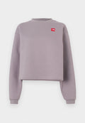 Lila kurz geschnittenes Sweatshirt mit langen Ärmeln, geripptem Rundhalsausschnitt und einem kleinen roten Logopatch auf der Brust. Weiches Material mit glatter Textur.