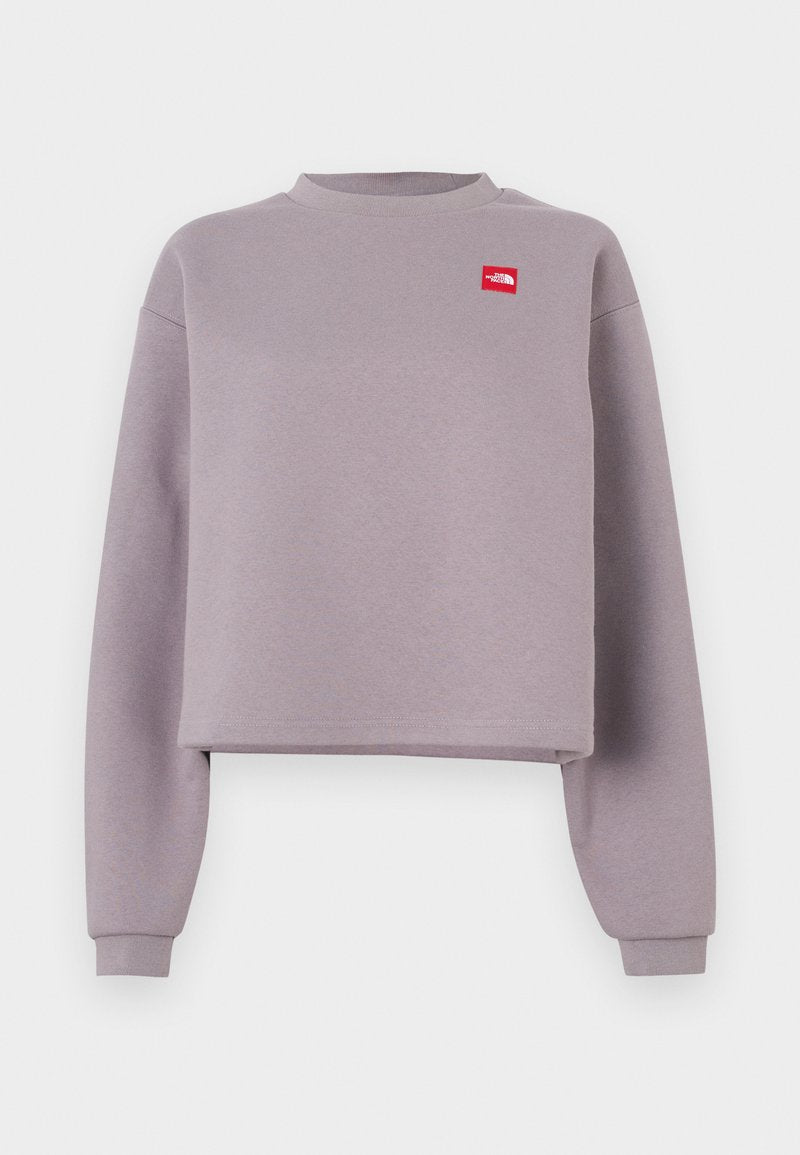 Lila kurz geschnittenes Sweatshirt mit langen Ärmeln, geripptem Rundhalsausschnitt und einem kleinen roten Logopatch auf der Brust. Weiches Material mit glatter Textur.