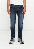 Ein Mann trägt blaue Slim-Fit-Jeans und weiße Sneakers mit schwarzen Schnürsenkeln und steht vor einem schlichten weißen Hintergrund.