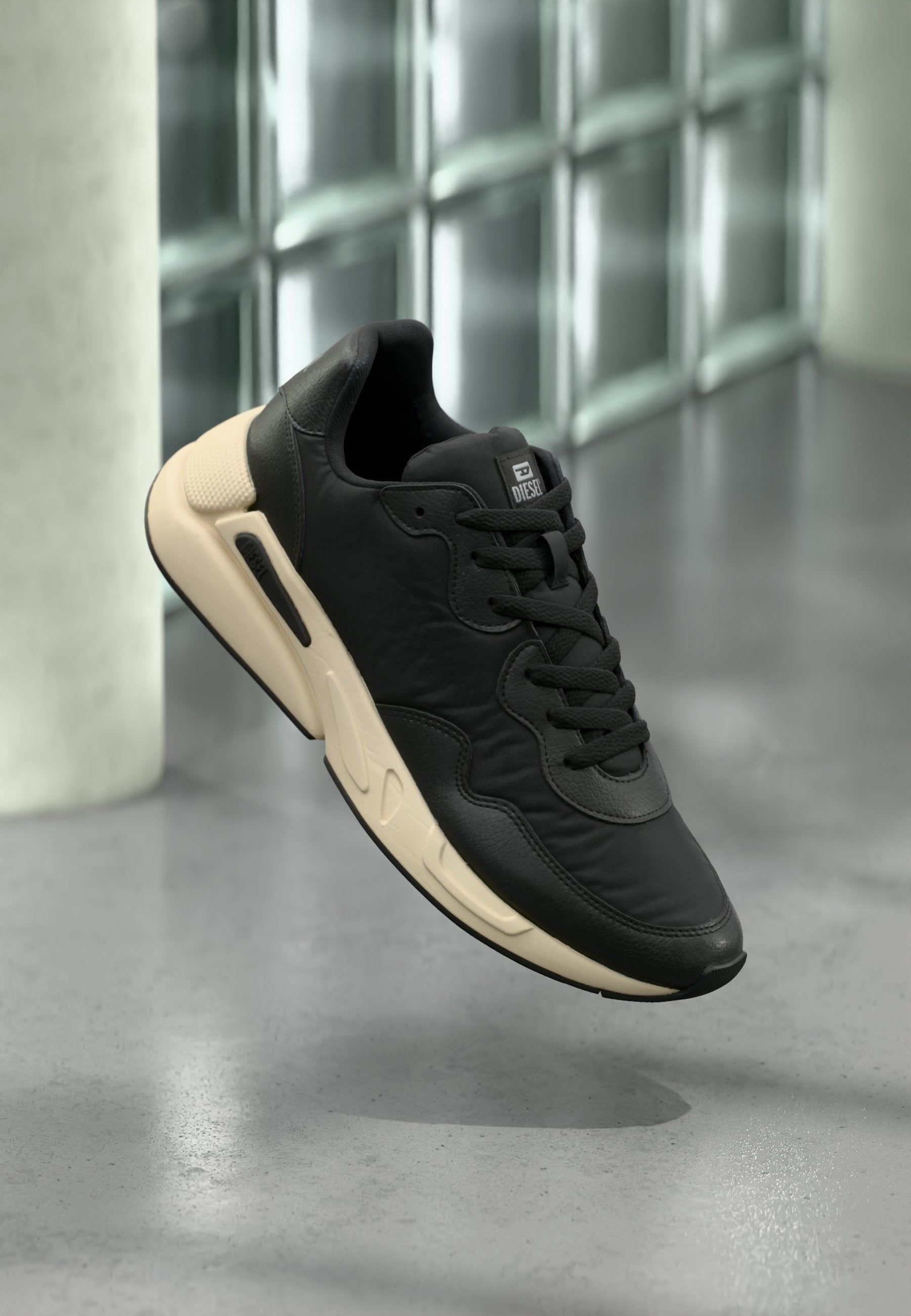 Schwarzer Sportschuh mit strukturiertem Lederobermaterial, dicker cremefarbener Sohle, abgerundetem Zehenbereich und dezentem Logodetail auf der Zunge.