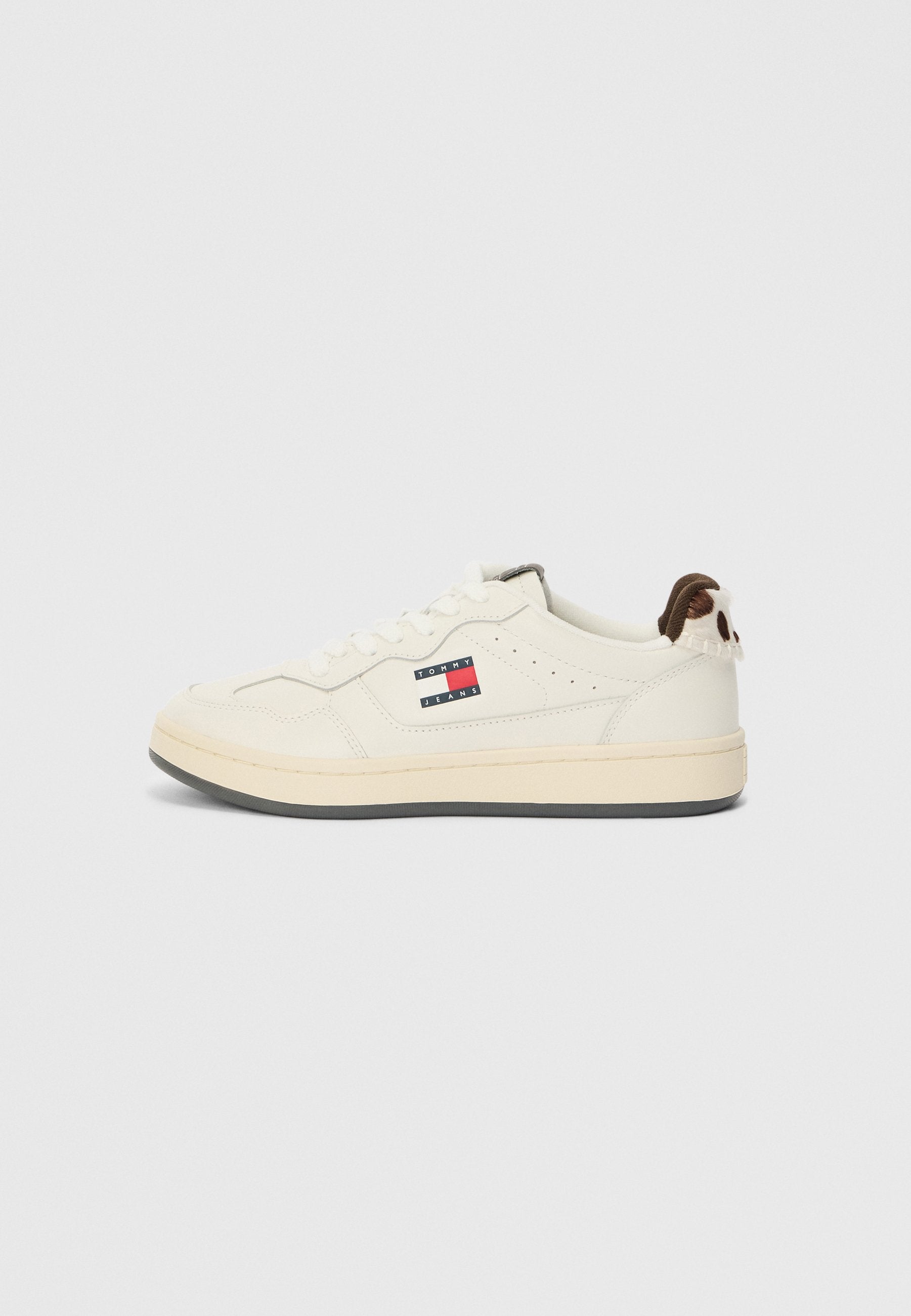 Weiße Sneaker mit einem glatten Lederoberteil, das mit einem Markenpatch in Rot, Weiß und Blau verziert ist, sowie einem strukturierten braunen Akzent an der Ferse.