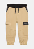 Beige Cargo-Hosen mit einem schwarzen Bund, der einen verstellbaren Kordelzug aufweist, seitlichen Taschen und einem auffälligen Patch mit der Aufschrift "HUGO". Elastische Bündchen an den Knöcheln.