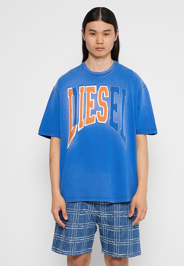 Blaues, oversized Baumwoll-T-Shirt mit "DIESEL" in großen orange- und weißen Buchstaben. Kombiniert mit karierten Jeansshorts. Einfache Hintergrund.