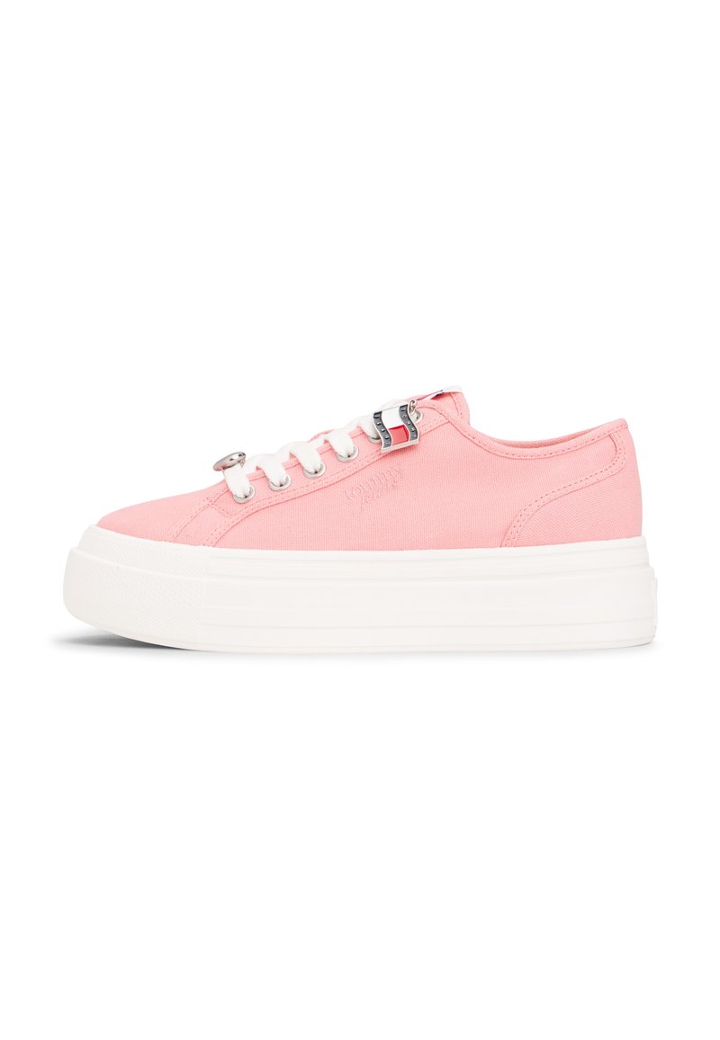 Pinkfarbener Canvas-Sneaker mit niedrigem Schaft, dicker weißer Plateausohle, weißen Schnürsenkeln und kleinen silbernen Metallösen, seitlich betrachtet.