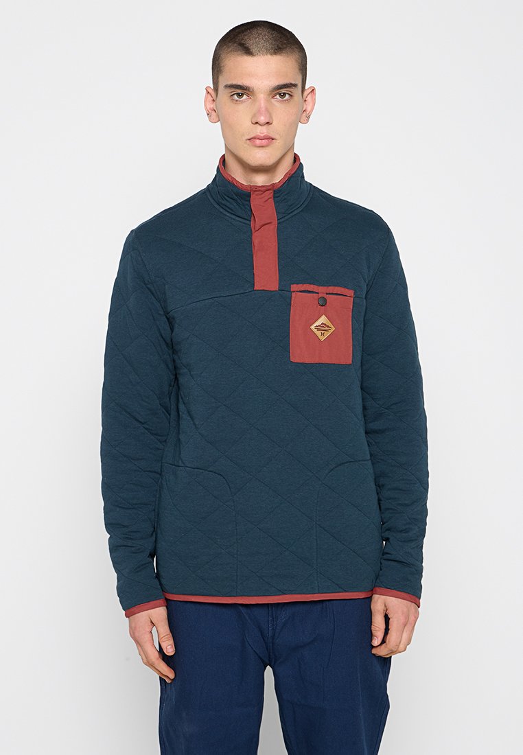 Gep quilteter Pullover in dunklem Teal mit einem Stehkragen und burgunderfarbenen Akzenten. Verfügt über eine Brusttasche mit Knopfdetail und Kängurutaschen.