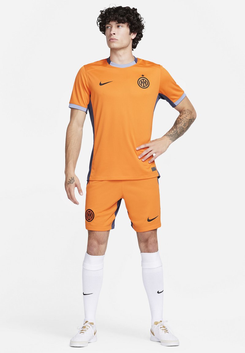 Orangenes Nike Fußballtrikot mit grauen Akzenten, ausgestattet mit einem Rundhalsausschnitt, Logo auf der Brust und passenden Shorts. Weiße Socken und Sneaker runden den Look ab.