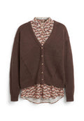 Braune, geknöpfte Strickjacke, die über einer floral gemusterten Bluse mit rosa, schwarz und cremefarbenen Farbtönen getragen wird, wobei Kragen und Saum sichtbar sind.