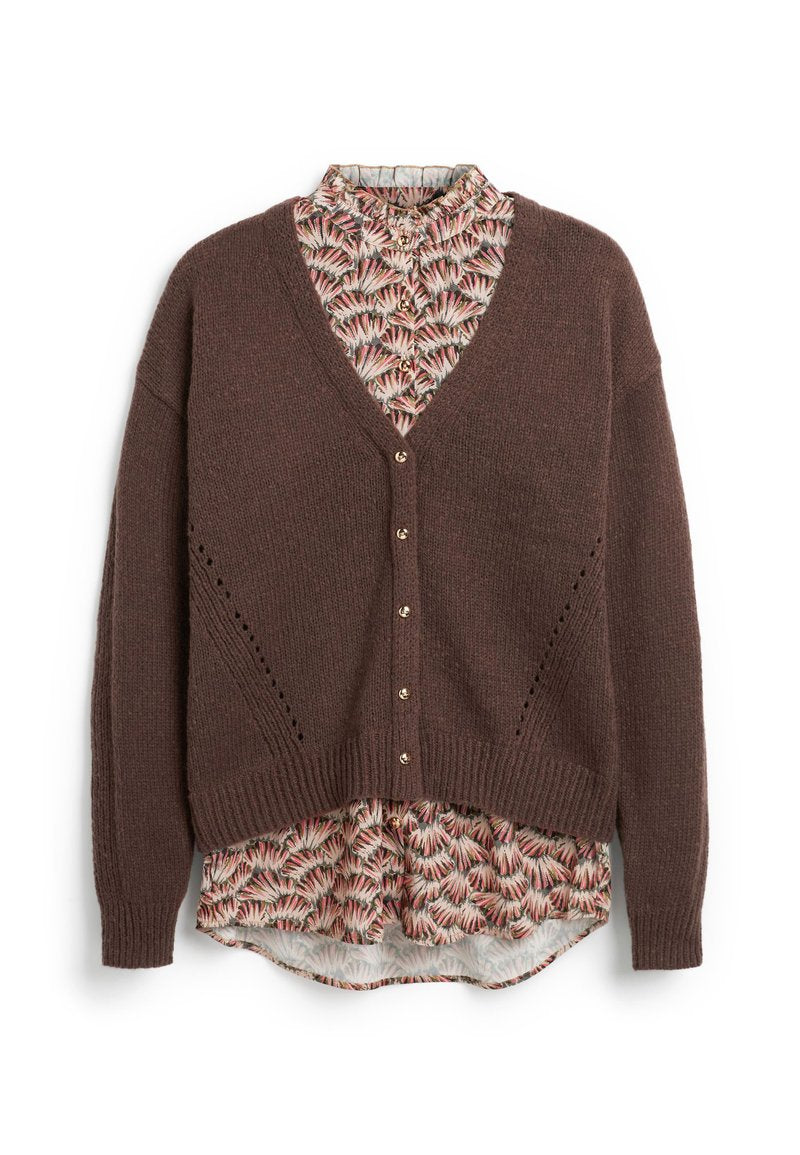 Braune, geknöpfte Strickjacke, die über einer floral gemusterten Bluse mit rosa, schwarz und cremefarbenen Farbtönen getragen wird, wobei Kragen und Saum sichtbar sind.