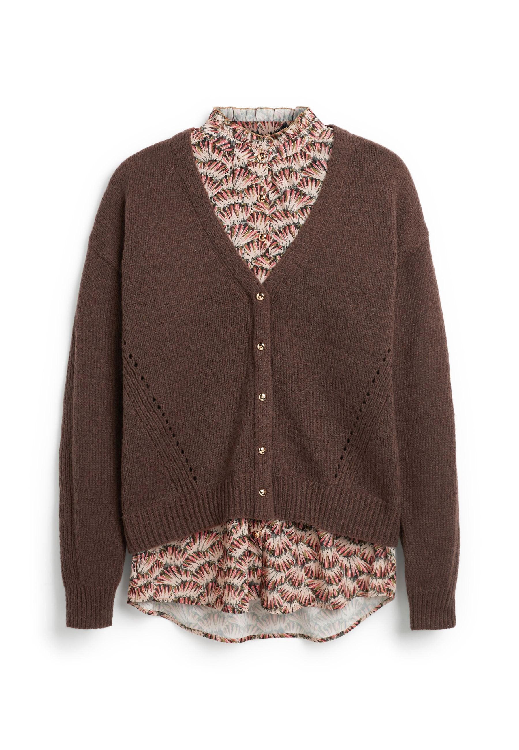 Braune, geknöpfte Strickjacke, die über einer floral gemusterten Bluse mit rosa, schwarz und cremefarbenen Farbtönen getragen wird, wobei Kragen und Saum sichtbar sind.