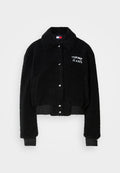 Schwarze, kurze Jacke aus flauschigem Material, mit durchgängiger Knopfleiste, Kragen und weißer "TOMMY JEANS"-Stickerei auf der Brust.