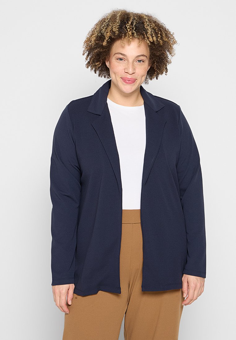 Marineblauer langer Blazer mit weicher Textur, offenem Frontdesign und Reverskragen, getragen über einem weißen Oberteil und braunen Hosen.