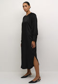 Schwarzes Satin-Kleid mit langen Ärmeln, rundem Halsausschnitt, seitlichen Schlitzen und geknöpften Manschetten. Kombiniert mit schwarzen Slingback-High Heels.