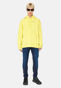 Gelbes Kapuzensweatshirt mit Fronttasche, kombiniert mit dunklen Slim-Fit-Jeans und schwarzen Sportschuhen. Das Modell trägt Sonnenbrillen.