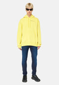 Gelbes Kapuzensweatshirt mit Fronttasche, kombiniert mit dunklen Slim-Fit-Jeans und schwarzen Sportschuhen. Das Modell trägt Sonnenbrillen.