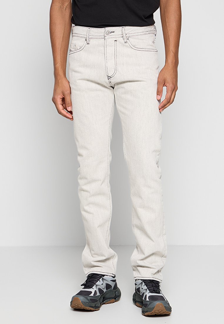 Hellgraue Jeans mit Slim Fit, ausgestattet mit fünf Taschen, Gürtelschlaufen und kontrastierenden Nähten, kombiniert mit schwarzen und grauen Sportschuhen.